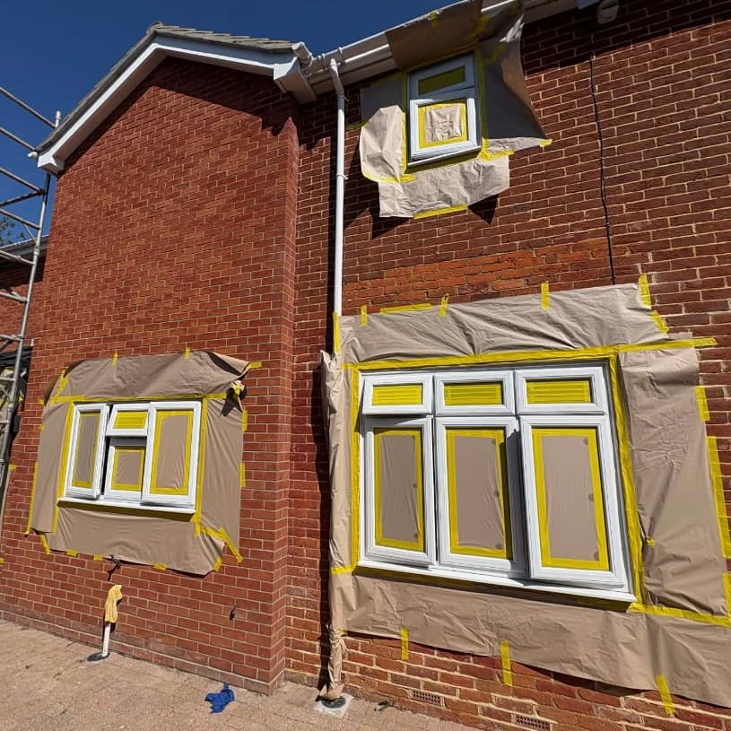 Red brick house with windows fully masked in preparation for UPVC spraying