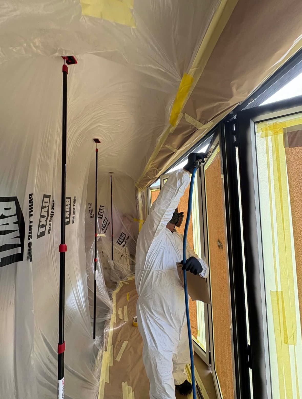 Newlook operator spraying inside a fully masked room with containment sheeting